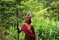 Portrait of old indigenous man with traditional clothes and plumes headdress with spear, blurred jungle forest background focus o