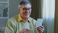 Portrait old man ecstatic grandpa with glasses sits at home indoors receives envelope letter postcard with good news Royalty Free Stock Photo