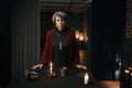 Portrait of old mature gypsy witch standing at table with psychic tools