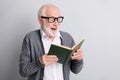 Portrait of old white hair impressed man read book wear spectacles dark sweater isolated on grey background Royalty Free Stock Photo