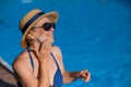 Portrait of an old woman in a straw hat, sunglasses and a swimsuit applying sunscreen to her face while relaxing by the Royalty Free Stock Photo