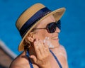 Portrait of an old woman in a straw hat, sunglasses and a swimsuit applying sunscreen to her face while relaxing by the Royalty Free Stock Photo