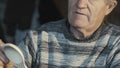 Portrait of old wrinkled carpenter hews wooden spoon and smiling at camera