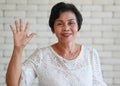 Portrait of an older senior Asian woman with a smiling face rises hand and waving for greeting Royalty Free Stock Photo