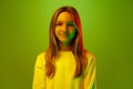 Portrait of one smiling pretty little girl, pupil dressed casually against green studio background in mixed neon light Royalty Free Stock Photo