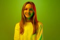 Portrait of one smiling with teeth pretty little girl dressed casually against green studio background in mixed neon Royalty Free Stock Photo