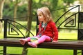 Portrait of a one year old cute little curly girl wearing red cardigan and a headband with a bowl sitting on a bench in the park Royalty Free Stock Photo