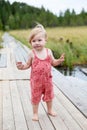 Portrait of a one-year-old girl standing on a wooden footbridge on a pier by the river Royalty Free Stock Photo