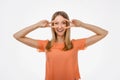 Portrait of optimistic blond girl showing peace sign over eye and smiling white background. Just be cool about it