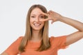 Portrait of optimistic blond girl showing peace sign over eye and smiling, white background. Just be cool about it