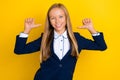 Portrait of optimistic confident schoolgirl with long hairstyle dressed blue jacket directing herself isolated on yellow