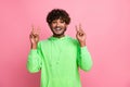 Portrait of optimistic funky arabian model man wear green trendy sweatshirt show double v sign isolated on pastel pink