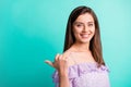 Portrait of optimistic funky brunette girl pointing back empty space wear purple shirt isolated on blue color background Royalty Free Stock Photo