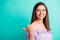 Portrait of optimistic funky brunette girl pointing back look empty space wear purple shirt isolated on blue color