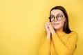 Portrait of optimistic glad young woman in eyeglasses with cheerful expression, touches cheeks, looks aside, dressed in sweater