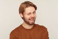 Portrait of optimistic happy young man with neat hair and beard wearing sweatshirt winking to camera