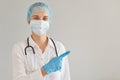 Portrait of optimistic woman doctor wearing medical cap, gloves and protective mask standing pointing aside with index finger, Royalty Free Stock Photo