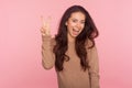 Portrait of optimistic wondered young woman with brunette wavy hair showing peace or victory gesture, making v sign Royalty Free Stock Photo