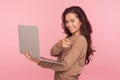 Portrait of optimistic young woman in casual sweater holding laptop, pointing finger to camera and smiling Royalty Free Stock Photo