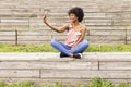 portrait outdoors of a beautiful young afro american woman at sunset using mobile phone. wood background. Lifestyle.Sitting on Royalty Free Stock Photo