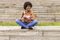 portrait outdoors of a beautiful young afro american woman at sunset using mobile phone. wood background. Lifestyle.Sitting on Royalty Free Stock Photo