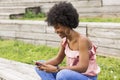 portrait outdoors of a beautiful young afro american woman at sunset using mobile phone. wood background. Royalty Free Stock Photo