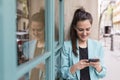 Portrait outdoors of young happy blogger woman with mobile phone. Glass windows background. Wearing casual clothes. Fun and Royalty Free Stock Photo