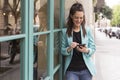 Portrait outdoors of young happy blogger woman with mobile phone. Glass windows background. Wearing casual clothes. Fun and Royalty Free Stock Photo