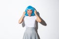 Portrait of outraged asian woman in blue wig looking mad, yelling at someone, standing over white background