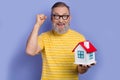 Portrait of overjoyed ecstatic pensioner wear yellow t-shirt in glasses win new house in lottery isolated on violet Royalty Free Stock Photo