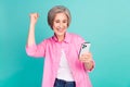 Portrait of overjoyed ecstatic woman with gray hair look at smartphone raising fist up win gambling isolated on teal Royalty Free Stock Photo