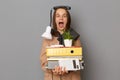 Portrait of overjoyed young pretty woman wearing beige jacket holding documents and her office stuff posing isolated over gray Royalty Free Stock Photo