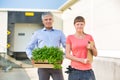 Portrait of owner with crate standing by female botanist against plant nursery