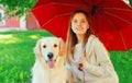 Portrait owner woman with Golden Retriever dog together hiding under red umbrella on grass