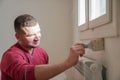 Portrait of painter young man in red t-shirt painting the wall in white color, with paint roller brush, home decor Royalty Free Stock Photo