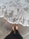 portrait of a pair of feet in the sand on the beach with beautiful foamy waves