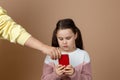 Portrait of parent taking smartphone away from girls hands, beige background. Little daughter hold tight phone and Royalty Free Stock Photo