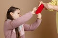 Portrait of parent taking smartphone out from girls hands, beige background. Angry daughter hold tight phone and oppose