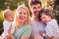 Portrait Of Parents Cuddling Baby Daughter And Young Son Outdoors In Garden In Evening Sun