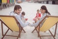 Portrait of parents relaxing on launge chairs with children playing in background Royalty Free Stock Photo