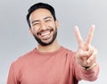 Portrait, peace sign and laughing Asian man in studio isolated on a gray background. Face, v emoji and happy, smiling or Royalty Free Stock Photo