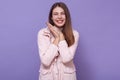 Portrait of peaceful joyful sweet young lady smiling sincerely, having cute smile, keeping hands together, being in good mood,