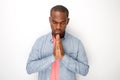 Peaceful young black man praying with hands clasp together by white wall