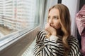 Portrait pensive blond pretty sad depressed woman on windowsill, looking distance. Lonely, tired, isolation. Close up