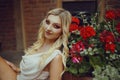 Portrait of a pensive blonde near red flowers. Professional makeup, red smoky eyes. Girl with a cute pretty face Royalty Free Stock Photo