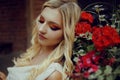 Portrait of a pensive blonde near red flowers. Professional makeup, red smoky eyes. Girl with a cute pretty face Royalty Free Stock Photo