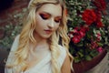 Portrait of a pensive blonde near red flowers. Professional makeup, red smoky eyes. Girl with a cute pretty face Royalty Free Stock Photo