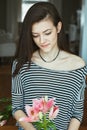 Pensive Caucasian young beautiful woman model with messy long hair in striped t-shirt at home with flowers