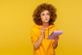 Portrait of pensive curly-haired hipster woman in urban style hoodie thinking over smart idea, holding pencil