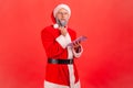 Portrait of pensive elderly man with gray beard wearing santa claus costume holding notebook in Royalty Free Stock Photo